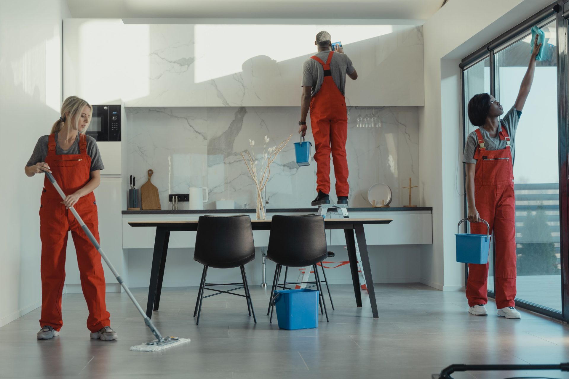 Eine Gruppe von Reinigungskräften in roten Uniformen wischt den Boden und putzt die Scheiben in einem modernen Speisesaal.